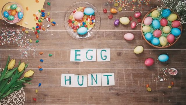 Man puts words Egg hunt on table decorated with easter eggs. Top view