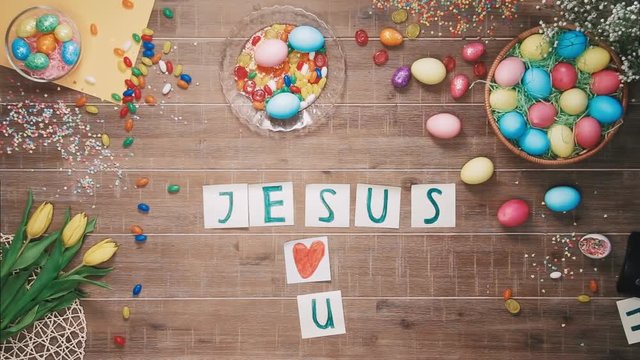 Man puts words Jesus Loves U on table decorated with easter eggs. Top view