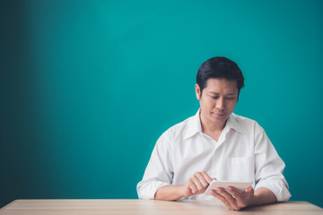 Portrait of businessman smiling and using pad at desktop against of blue wall. Vintage filtered image.