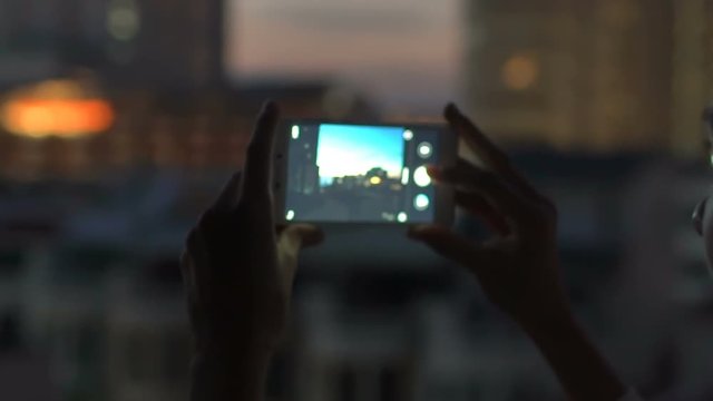 Slow motion of Closeup woman taking photo of cityscape view with smartphone in bar rooftop terrace at night
