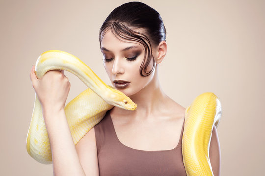 Beautiful brunette woman with a albine python. Fashion makeup, beige background