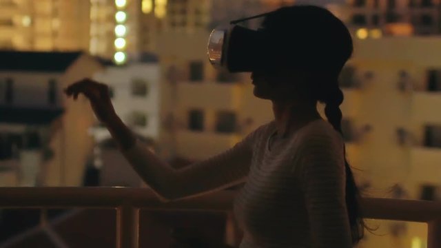 Slow motion of young woman on rooftop terrace using virtual reality headset and having VR experience at night