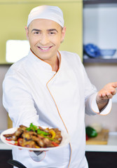 Cook holding plate with food in welcoming gesture