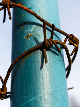 Rusty barbed wire around the painted steel pillar and blue sky