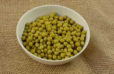 Canned low salt sweet peas in white bowl on burlap