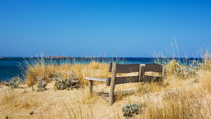 Fototapeta premium Bench on sea shore, covered with sand