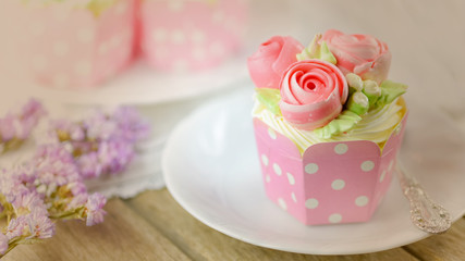 Vanilla cup cake and spoon on a plate with cup cake in background and flower  as decoration.