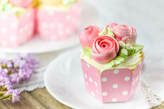 Vanilla cup cake and spoon on a plate with cup cake in background and flower  as decoration.