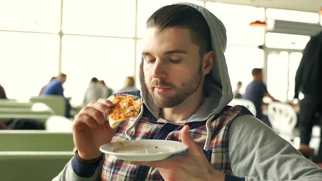 Handsome man in hood answers cellphone while eating pizza, steadycam shot

