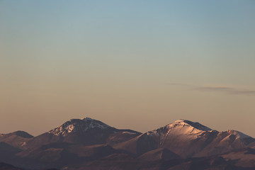 A minimalist view of some mountains top with snow, under a big, almost empty sky, with golden hour warm colors