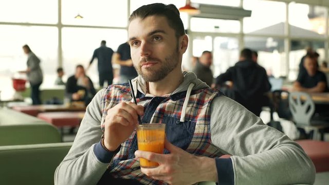 Happy man looks relaxed while drinking juice and chatting with someone in the cafe, steadycam shot
