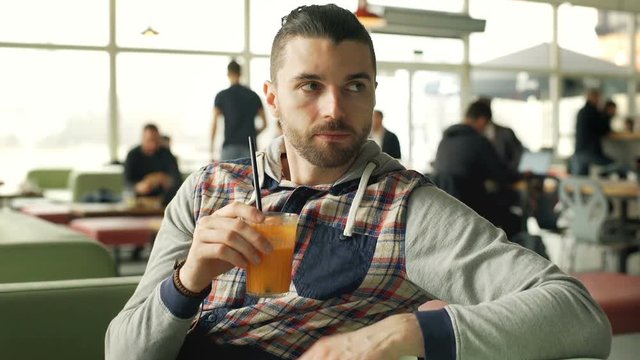 Handsome man drinking orange juice in the cafe and smiling to the camera, steadycam shot

