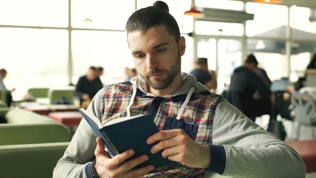 Man in hoodie answers cellphone while reading book in the cafe, steadycam shot
