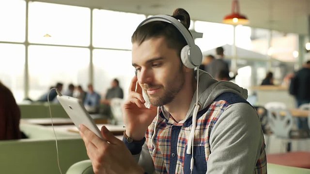 Hipster listening music on headphones in the cafe and smiling to the camera, steadycam shot
