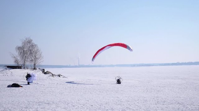 A male athlete flies across the sky on a paraglider, in winter, makes a landing on the snow. 4k. 3840x2160