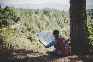 Young woman backpacker hiker reading map hiking trip looking away to find place to go. Adventure...