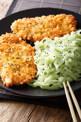 Asian food: steak in breaded Panko and green noodles with sesame close-up. Vertical