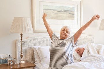 Senior woman waking up with a stretch in the morning  - obrazy, fototapety, plakaty