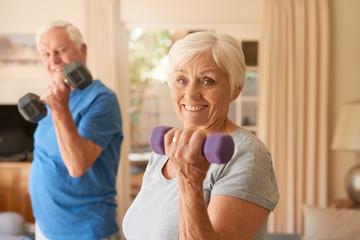 Smiling active senior couple lifting dumbells together at home