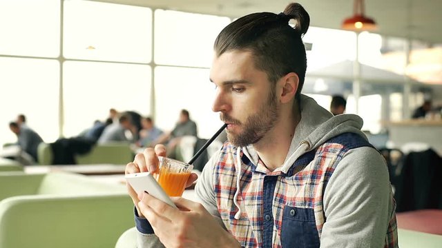 Man drinking orange juice and looks bored while browsing internet on smartphone, steadycam shot
