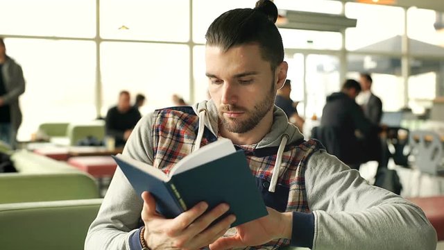 Handsome man in hoodie reading interesting book in the cafe, steadycam shot
