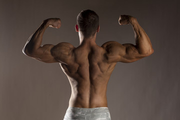 rear view of the half-naked handsome and muscular young man posing on a gray background