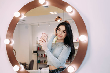 Woman makes selfie in makeup mirror with lamps