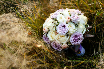 Tender wedding bouquet made of beige and violet roses lies on dry grass