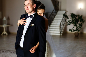 Bride leans to groom tender hugging him from behind in the room