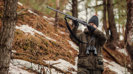 Naklejka premium male hunter ready to hunt, holding gun and walking in forest.