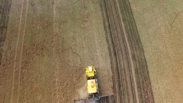 Aerial view of brown field with sowing machine. Growing and crop care on springtime. Agriculture from above. Seasonal work on Czech countryside. Czech Republic, Central Europe.