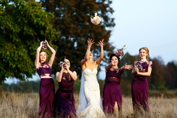 Laughing bride and bridesmaids play with bouquets standing on the backyard