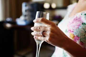 Woman in flowered dress holds champagne flute in arm with wedding ring