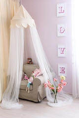 Interior of a child. Interior nursery for girl. A gently pink colored room, a comfortable armchair with a canopy above it, pink flowers and a lovely doll, huge love letters on the wall. Nobody.