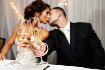 Bride and groom reach out their hands with champagne flutes while they kiss
