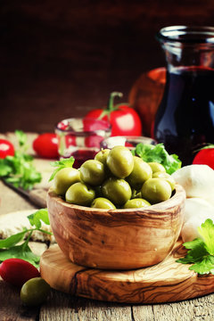 Green olives in a wooden bowl, selective focus