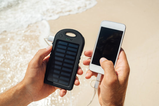Charger Solar in the hands of men on the background of the sandy beach. Charging smartphone phone from the solar battery.