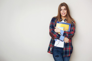 Portrait of young beautiful female student with books standing against wall.
