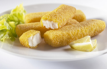 Breaded hake sticks with salad and lemon garnish on white plate and background