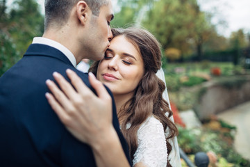 Fototapeta premium Groom kisses bride's forehead tender while she leans to him