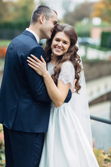 Obraz premium Pretty bride smiles while groom kisses her forehead hugging her