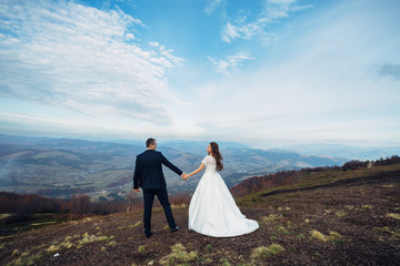 Look from behind at wedding couple watching autumn clouds on high hill