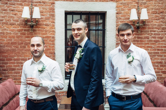 Profile of groom and groomsmen drinking whisky in brick hall