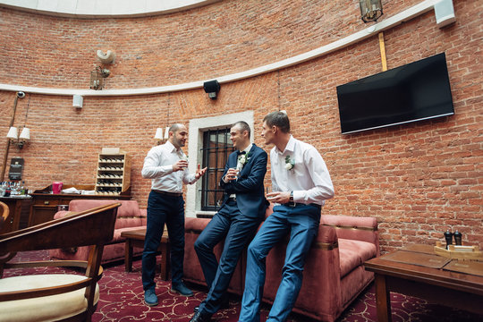 Funny groom and groomsmen drink whisky in the old brick hall