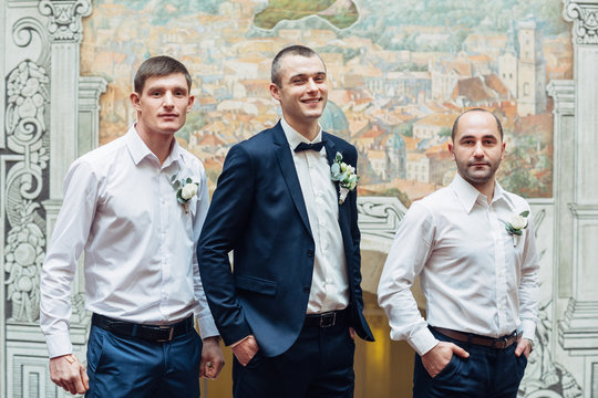 Groom and groomsmen stand side by side before wall with ancient paintings