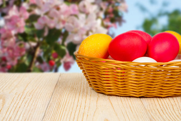 basket with easter eggs on aged table over blurred pink apple flowers