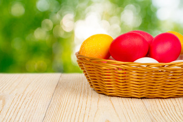 basket with easter eggs on aged table over blurred young foliage with sunbeam