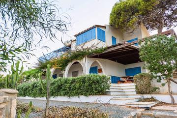 Classical architecture of the mediterranean cyprus, spaine, greek or italian white house with blue wooden windows and green trees, summer time