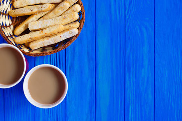 Two cups of cappuccino and italian bread sticks served in rustic basket on blue wooden table