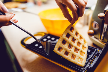 Waffle maker in the kitchen. Cook homemade waffles, Take out the prepared waffle - obrazy, fototapety, plakaty